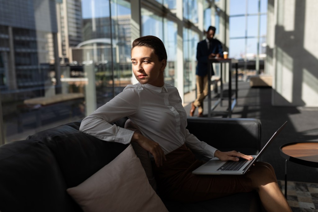Businesswoman with laptop sitting on the sofa and looking away in office