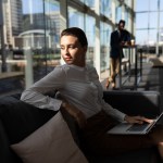 Businesswoman with laptop sitting on the sofa and looking away in office