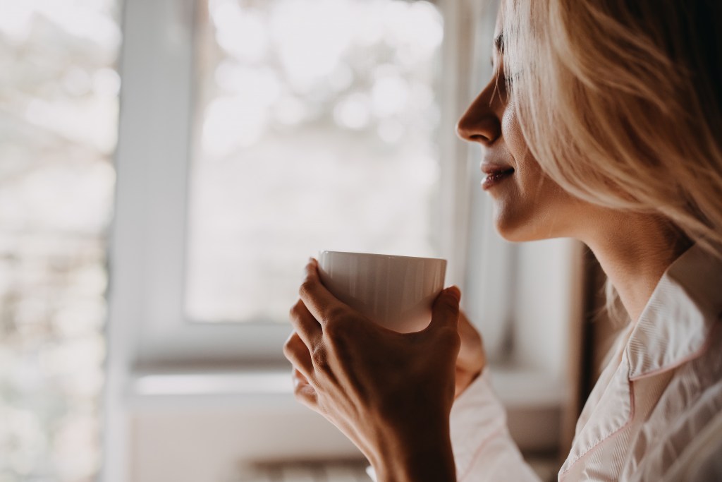 Woman holding a cup of coffee, sitting by the window in the morning.