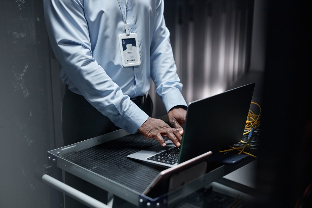 man typing on laptop in server room