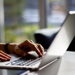 Girl typing on a laptop keyboard in a sunny interior, close up