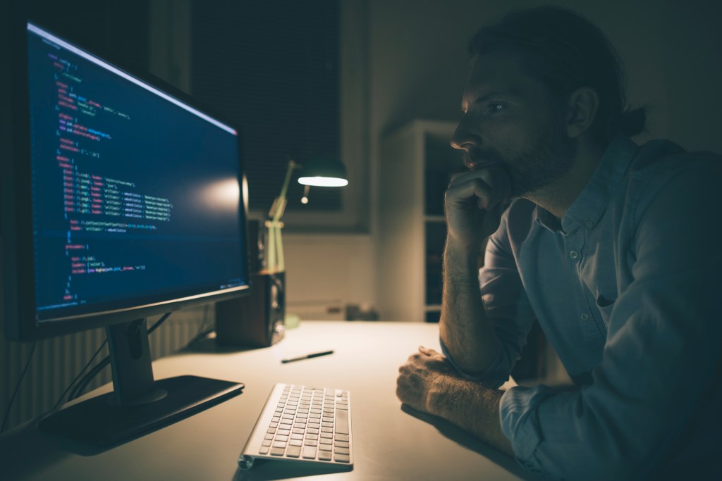 Man focused on reading computer codes. Programmer working late from his home office