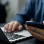 Man hand holding mobile smartphone digital technology network communications at desk.